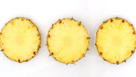 3-Ananas-Liegen-Auf-Einem-Weißen-Hintergrund,-Im-Hintergrund-Fallen-In-Zeitlupe-Wasserspritzer.